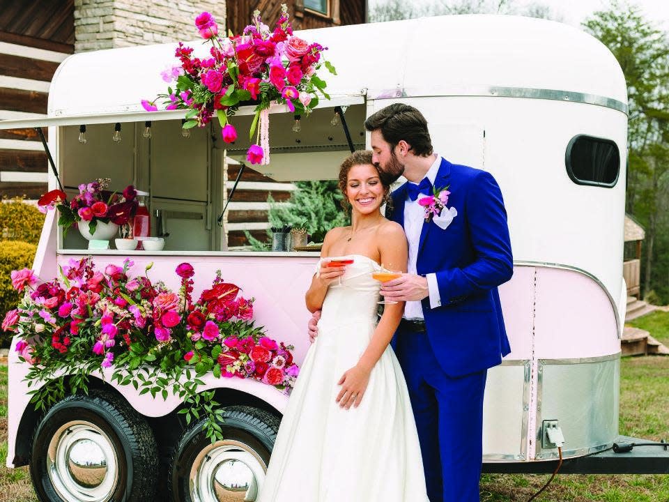 Newlyweds pose beside Morgan Pannell's mobile bar...a converted horse trailer decorated with colorful flowers.