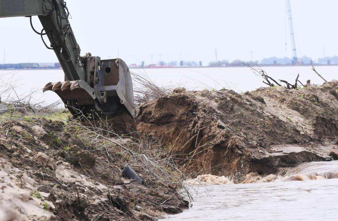 An excavator drops rock and dirt to stop the breach in the levee along Deer Creek Saturday afternoon, March 18, 2023.