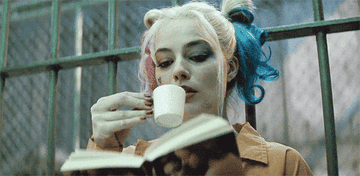 Harley Quinn delicately sips from an espresso cup while reading a book