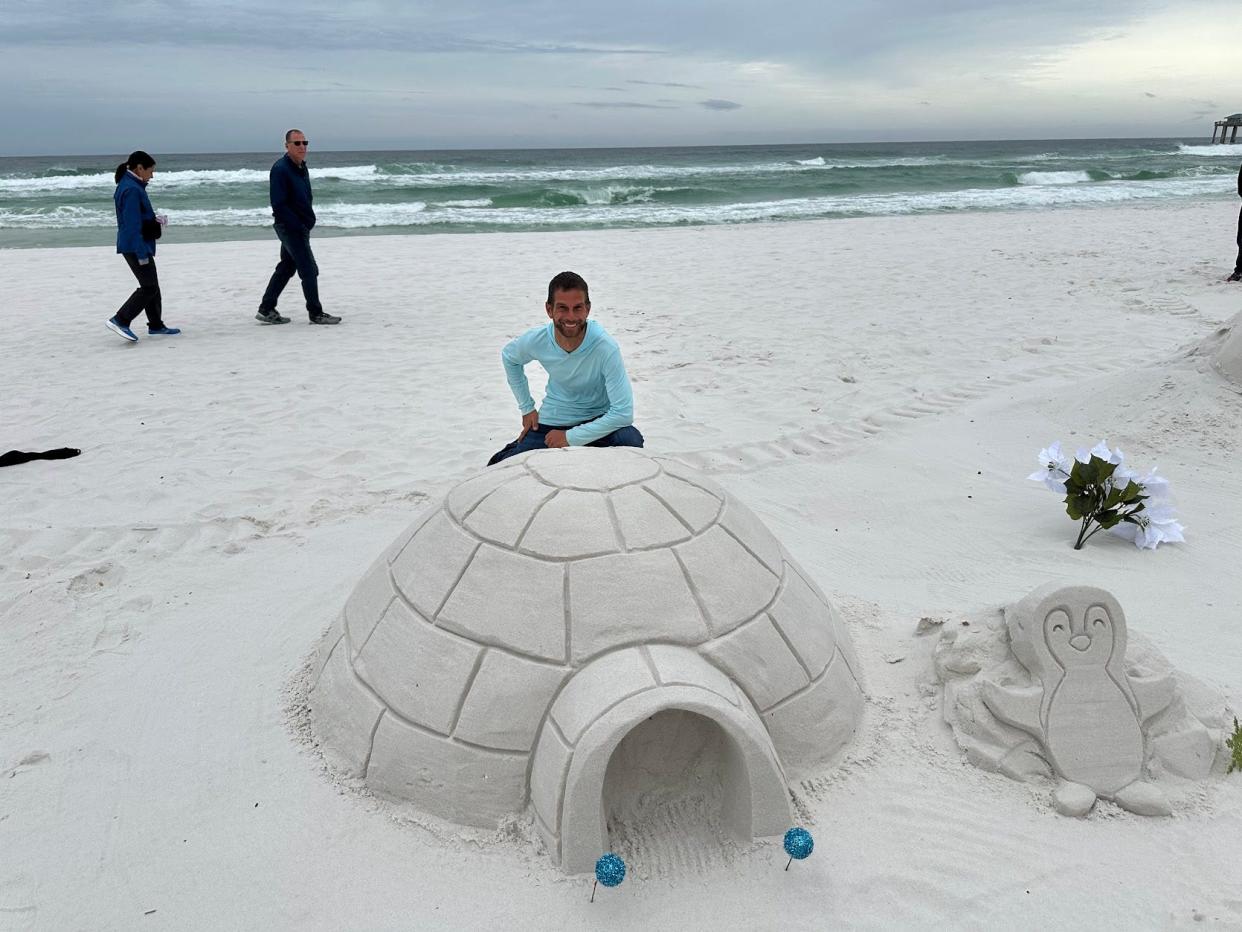 Jason Harwell of SandEffects kneels down behind his creation of an igloo and penguin.