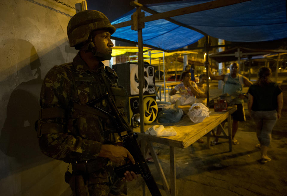 An Army soldier takes position while residents stand near him during an operation to occupy the Mare slum complex in Rio de Janeiro, Brazil, Saturday, April 5, 2014. More than 2,000 Brazilian Army soldiers moved into the Mare slum complex early Saturday in a bid to improve security and drive out the heavily armed drug gangs that have ruled the sprawling slum for decades. (AP Photo/Silvia Izquierdo)