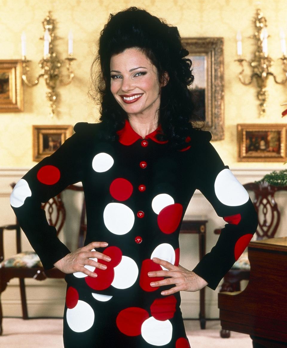 Fran Drescher smiles with hands on hips, wearing a long-sleeved dress with large white and red polka dots