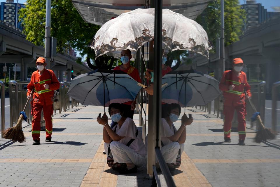 people wait at bus station with umbrellas on a sunny day