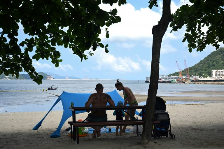 Una familia se sienta a la sombra de un árbol tras refrescarse en una playa de Hong Kong durante un día caluroso, el 21 de junio de 2024 en la ciudad china (Peter Parks)