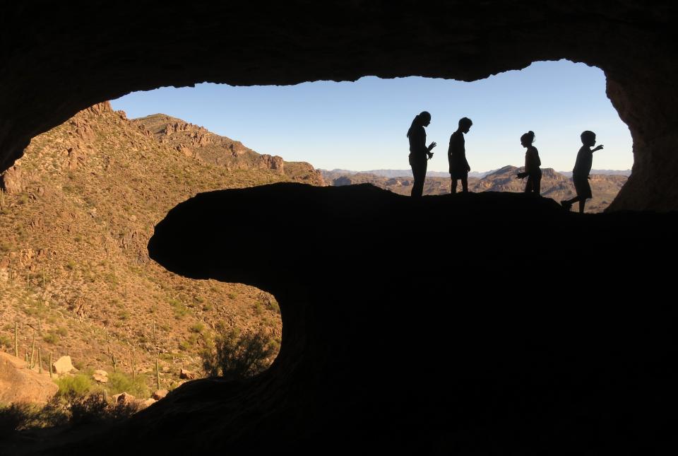 People are silhouetted as they look out onto the Superstition Mountains from inside the Wave Cave in the Superstition Wilderness Area outside of Gold Canyon.