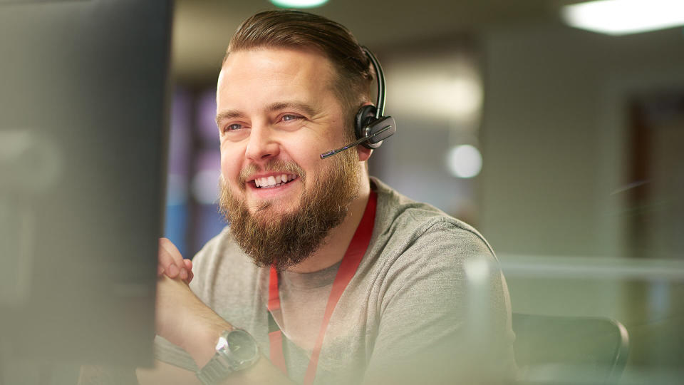 a call centre phone operative in his mid 30s chats on the phone at his desk .