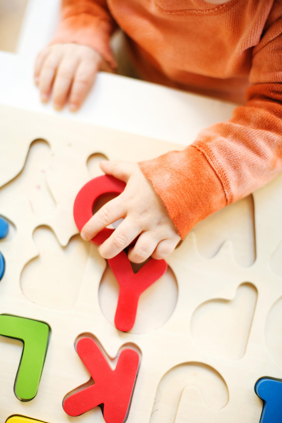 Child's hand solving a wooden puzzle, placing a red piece