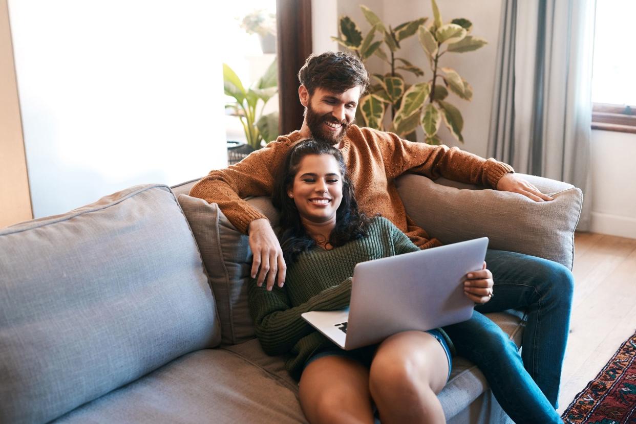 young couple using a laptop while relaxing on the sofa at home