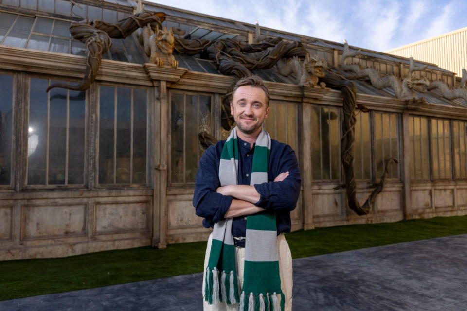 Felton smiling and wearing a scarf while standing with hands folded