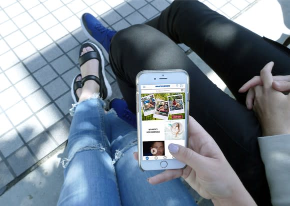 A woman holding a smartphone displaying Skechers' site.