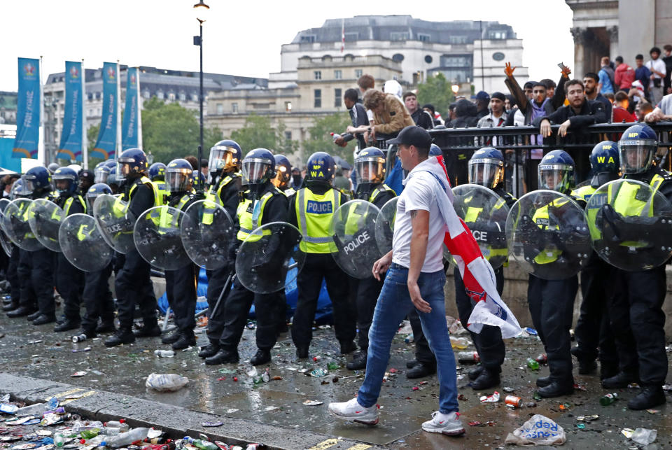 FILE - An England supporter wears a flag as he walks by a police line near Leicester Square in London, Sunday, July 11, 2021, during the Euro 2020 soccer championship final match between England and Italy which is being played at Wembley Stadium. An investigation into the disorder at the European Championship final says aggression by England fans exposed an “embarrassing” part of the national culture that endangered lives and should lead to entry to stadiums being prohibited to anyone chanting abuse and high on drugs or drunk. (AP Photo/Peter Morrison, File)