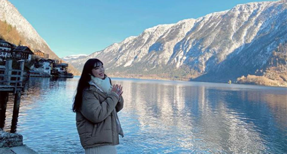 A woman poses for a photo at the Hallstatt waterfront with the mountains behind her.