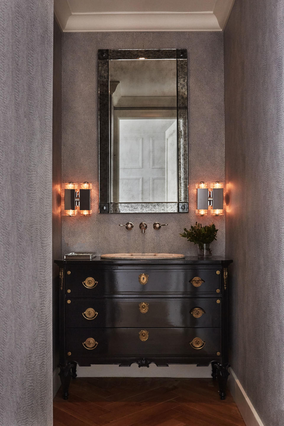 The vintage sink—a marble piece from the 1930s—is one of the only objects Blinken kept from the original apartment. The vanity is a refurbished chest from an antiques store. Inspired by a friend’s snakeskin clutch, Blinken sourced the custom lizard print wallpaper to add a textural note to the powder room. The lights are from Olde Good Things.