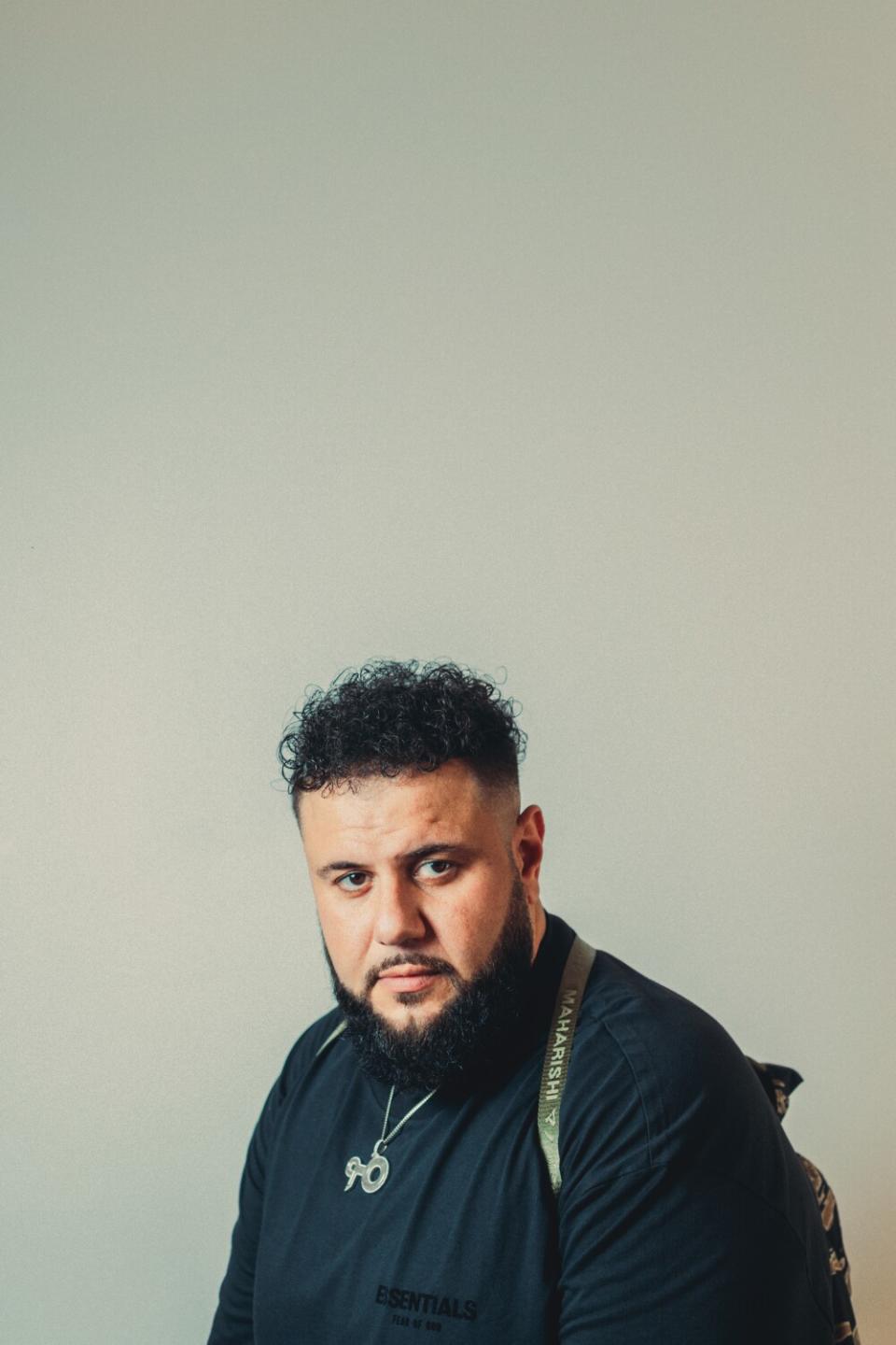 A man wearing a black shirt, backpack and necklace