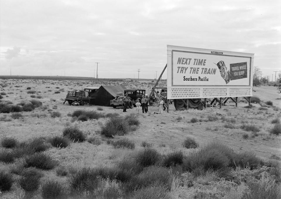 Fotografía de Dorothea Lange durante la Gran Depresión. Tres familias acampan en las llanuras a lo largo de la carretera U.S. 99 en California. Están acampadas detrás de una valla publicitaria que sirve de cortavientos parcial. Todos necesitan trabajo. 1938. La valla publicitaria dice: ‘La próxima vez prueba el tren. Southern Pacific. Viaje mientras duerme’. <a href="https://commons.wikimedia.org/wiki/File:LangeNextTimeTryTheTrain.jpg" rel="nofollow noopener" target="_blank" data-ylk="slk:Library of Congress;elm:context_link;itc:0;sec:content-canvas" class="link ">Library of Congress</a>