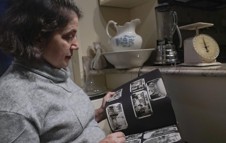 Anne D'Innocenzio scrolls through a family album inside her kitchen, surrounded by momentos from her childhood home, including a working blender from the 1960s and an old food scale from the 1940s, Monday Feb. 26, 2024, in New York. (AP Photo/Bebeto Matthews)