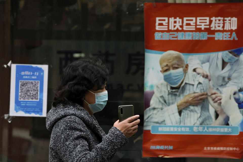 A woman wearing a face mask walks by a poster promoting the COVID-19 vaccination at a community health center in Beijing, Wednesday, Oct. 26, 2022. The Chinese city of Shanghai started administering an inhalable COVID-19 vaccine on Wednesday in what appears to be a world first. (AP Photo/Andy Wong)