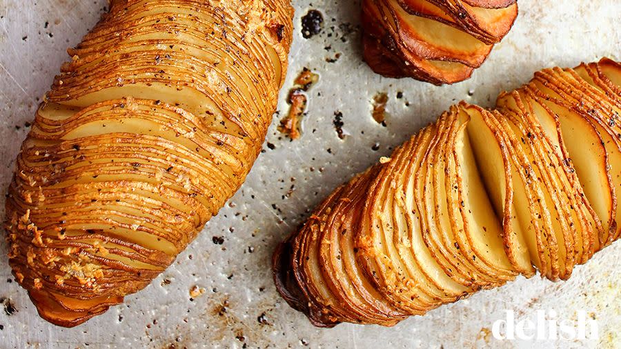freshly baked hasselback potatoes are golden brown and glistening on a silver sheet tray, topped with black pepper and salt