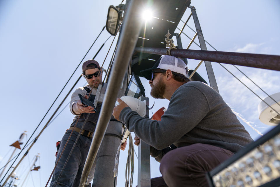 Mark Hager, right, and Anthony Lucia, install a camera aboard the Sabrina Maria fishing vessel in Gloucester, Mass., May 11, 2022. Hager's Maine-based startup, New England Maritime Monitoring, is one of a bevy of companies seeking to help commercial vessels comply with new federal mandates aimed at protecting dwindling fish stocks. But taking the technology overseas, where the vast majority of seafood consumed in the U.S. is caught, is a steep challenge. (AP Photo/David Goldman)