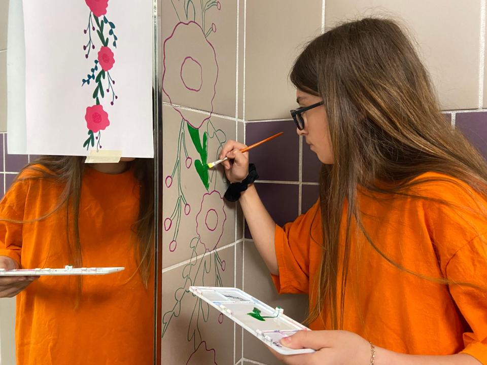 Student paints mural in girls' bathroom at Spradling Elementary.