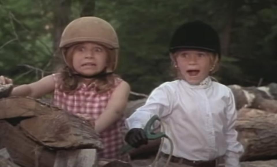 Ashley Olsen stands next to Mary-Kate Olsen who holds a slingshot. They both grimace, looking shocked.