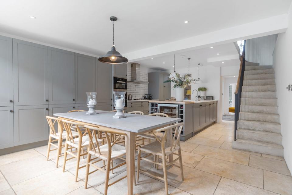 an image of the property's modern open plan kitchen featuring a wine cooler and island as well as a grey eight seater wooden dining set