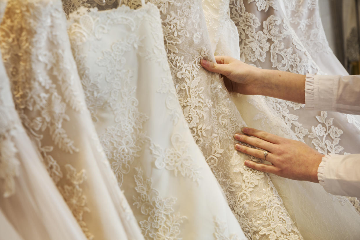 Rows of wedding dresses on display in a specialist wedding dress shop. Close up of full skirts, some with a lace overlay, in a variety of colour tones. .