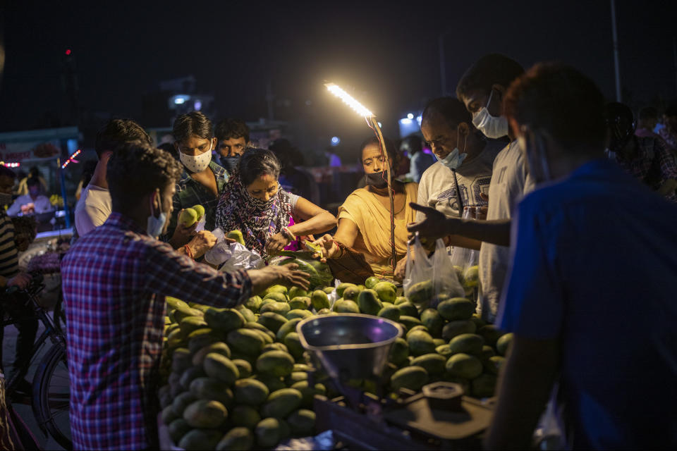 People wearing masks as a precaution against the coronavirus crowd a mango seller's stall at a daily evening market in Noida, outskirts of New Delhi, India, Thursday, July 16, 2020. (AP Photo/Altaf Qadri)