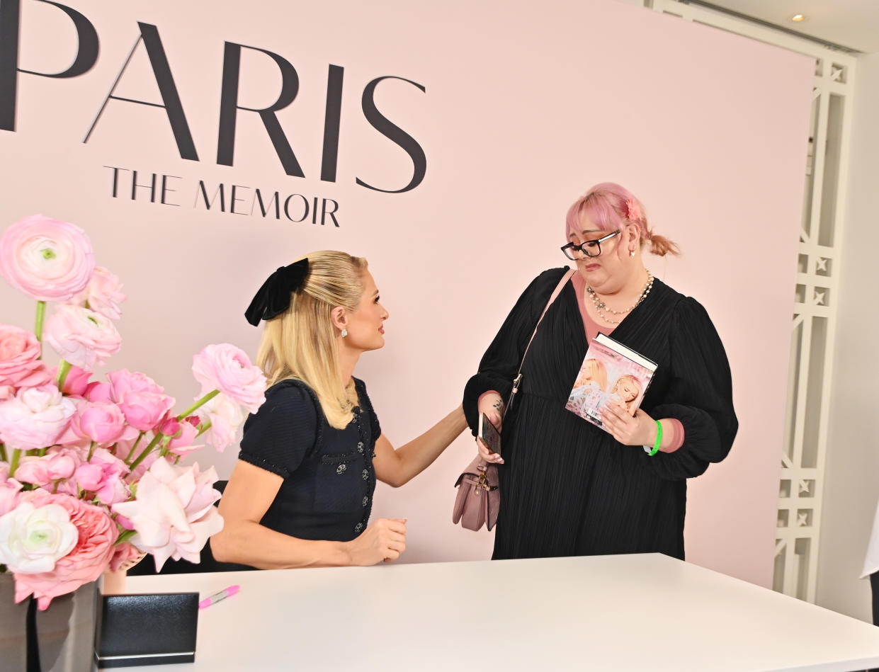 Paris Hilton, seated, touches the arm of a fan standing next to her at a book signing in the United Kingdom.