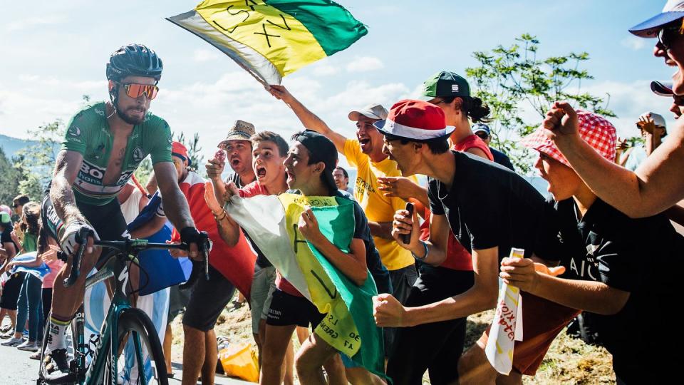 a group of fans holding a flag and cheering as sagan climbs part them