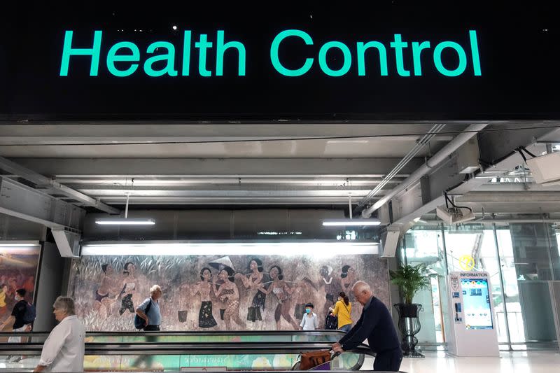 Tourists are seen next to a health control sign at Bangkok's Suvarnabhumi international airport in Thailand