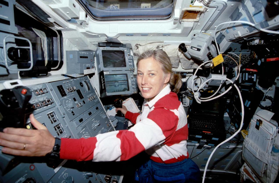 a woman gripping two joysticks at a control panel. she wears the shirt as where's waldo.