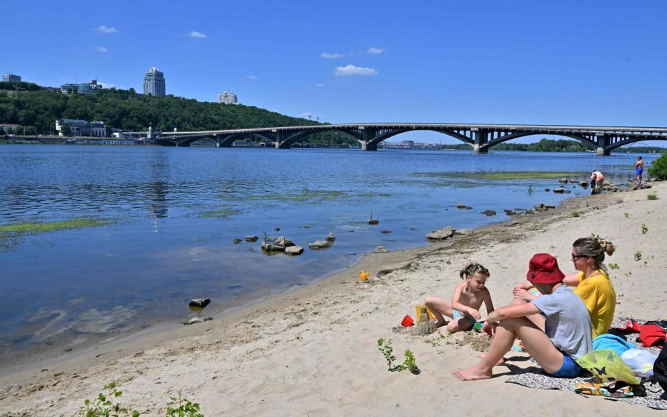 A family sits on the sandy shores of the Dnipro river that runs through the Ukrainian capital of Kyiv - SERGEI SUPINSKY 