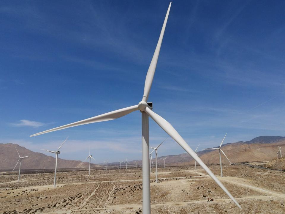 wind turbine in a field of turbines against blue sky mountains in the background