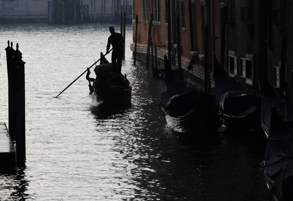 A gondolier navigates the waterways in Venice, Italy, Saturday, Jan. 30, 2021. Gondolas and other vessels are moored instead of preparing for Carnival's popular boat parade in the lagoon. Alleys are eerily empty. Venetians and the city's few visitors stroll must be masked in public places, indoors and out, under a nationwide mandate. (AP Photo/Antonio Calanni)