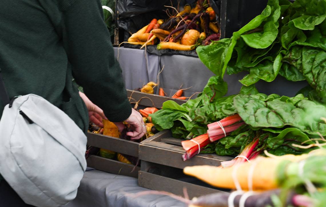 A customer reaches for carrots grown at De La Mesa Farms at the farm’s booth at the Proctor Farmers Market on Aug. 10, near Tacoma. De La Mesa is a no till farm that has used cover crops for ten years.