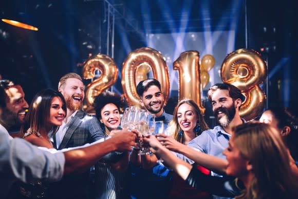 A group of young people toasting with champagne glasses, with a 2018 balloon in the background