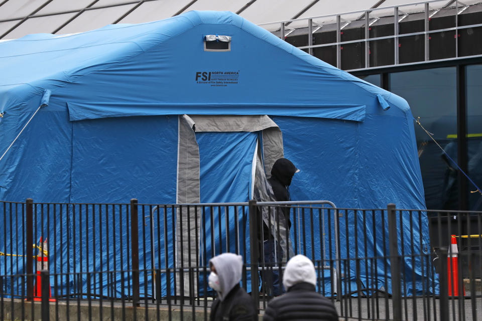 A person emerges from a tent set up in the driveway of the emergency entrance to Elmhurst Hospital Center in New York, Saturday, March 28, 2020, as others wait in line to be tested for coronavirus. The hospital is caring for a high number of coronavirus patients in the city. (AP Photo/Kathy Willens)