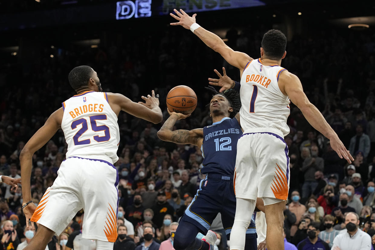 Memphis Grizzlies guard Ja Morant scores against between Phoenix Suns guard Devin Booker (1) and forward Mikal Bridges (25) in the last second of an NBA basketball game, Monday, Dec. 27, 2021, in Phoenix. Memphis won 114-113. (AP Photo/Rick Scuteri)