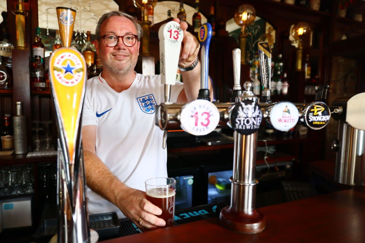 A bartender wearing an England football shirt pours a pint at a pub  (Getty Images)