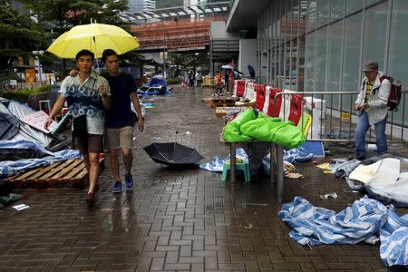 One of the remaining pro-democracy protester (R) packs his belongings as two others carrying a yellow umbrella, the symbol of the Occupy Central movement, walk past outside the government headquarters in Hong Kong, China June 24, 2015. REUTERS/Bobby Yip