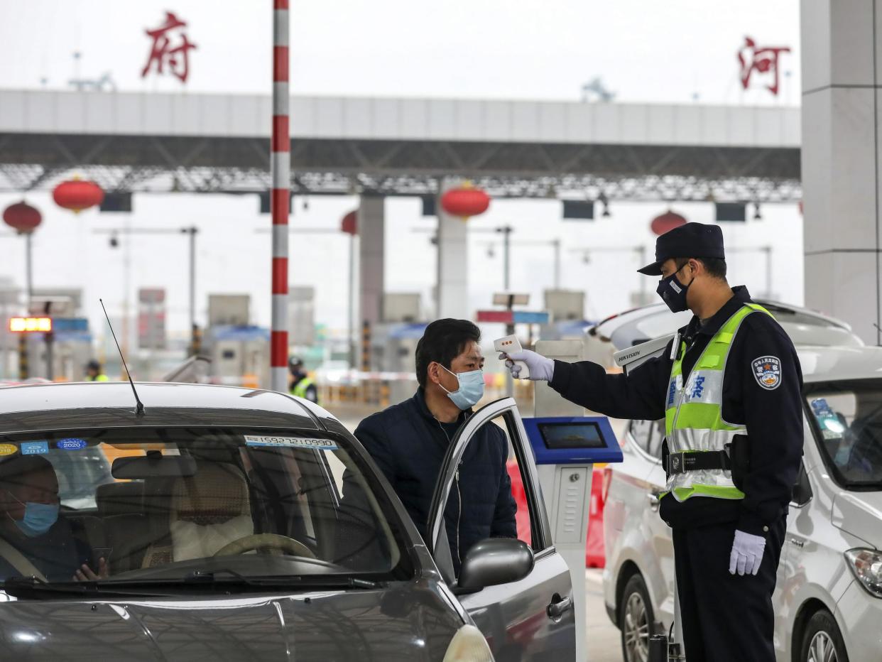 A police officer checks a driver's temperature at a roadblock outside the quarantined city of Wuhan: AP