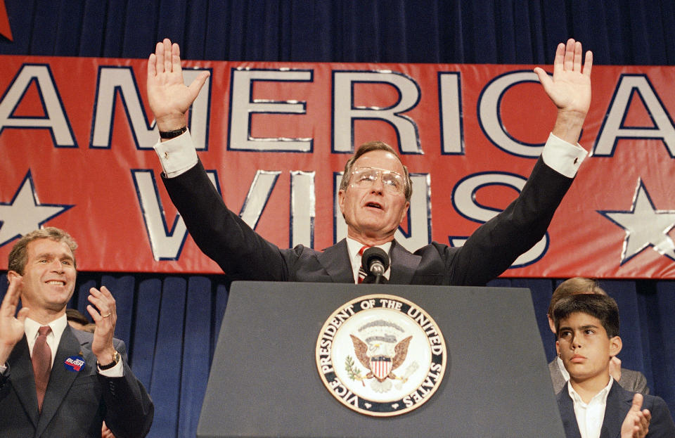 FILE - In this Nov. 9, 1988 file photo, President-elect George H. W. Bush holds his hands up to acknowledge the crowds applause, and ask them to allow him to continue his speech, during his victory rally with grandson, George P. Bush, right, and son George W. Bush, left, in Houston, Texas. The Kennedys had their New England coastal hideaway in Hyannis Port, a Camelot-like mystique and a political godfather in Joseph P. Kennedy. For the country's other political dynasty, the Bushes , it was a summer home in Maine and the West Texas oil patch that created a mix of Yale blue-blood and backcountry cowboy. Their patriarch was George H.W. Bush, a World War II hero, Texas congressman, the director of the CIA, vice president and eventually president. (AP Photo, File)