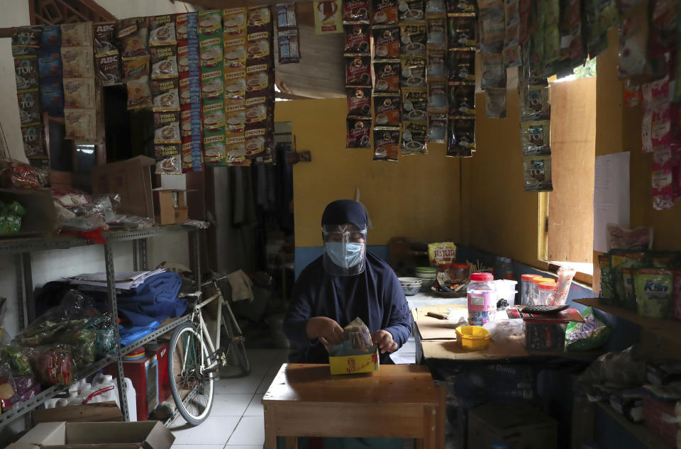 A shop owner wearing a face shield counts money as she waits for customers in Tangerang, Indonesia, Monday, Nov. 23, 2020. (AP Photo/Tatan Syuflana)