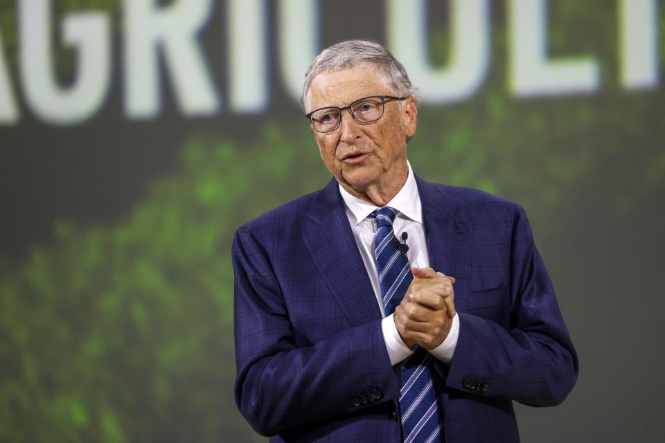 Bill Gates wearing a navy blue suit with his hands cusped together