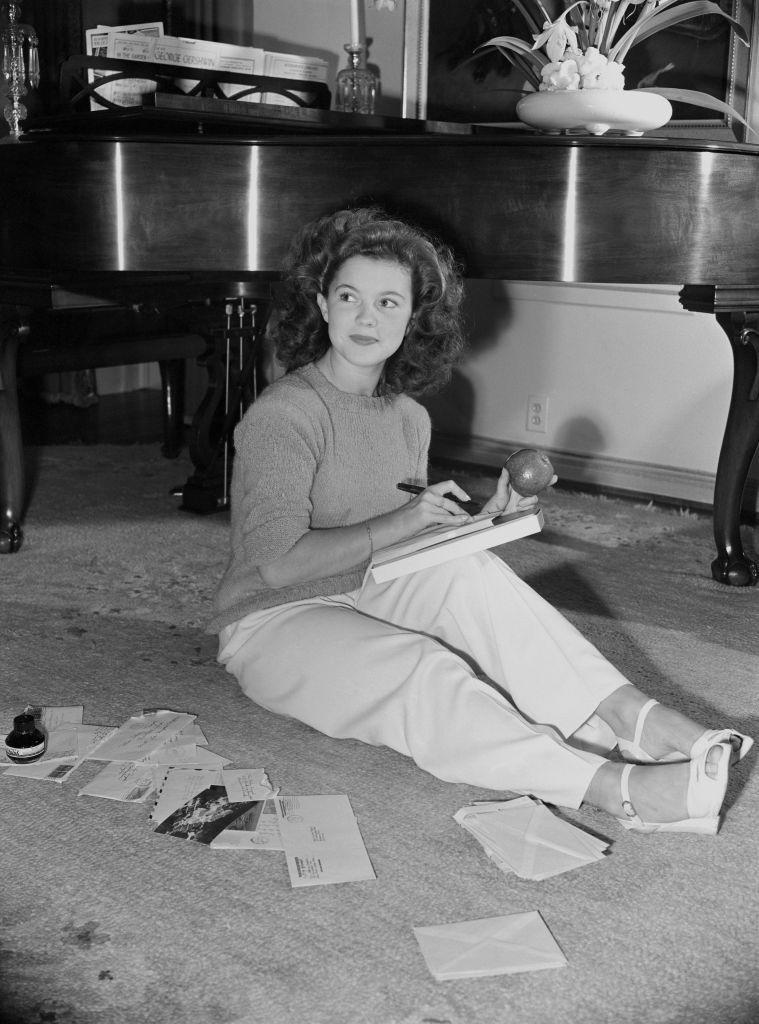 <p>The former child star takes a moment to read some mail and enjoy an apple on the floor of her Los Angeles living room, circa 1944.</p>