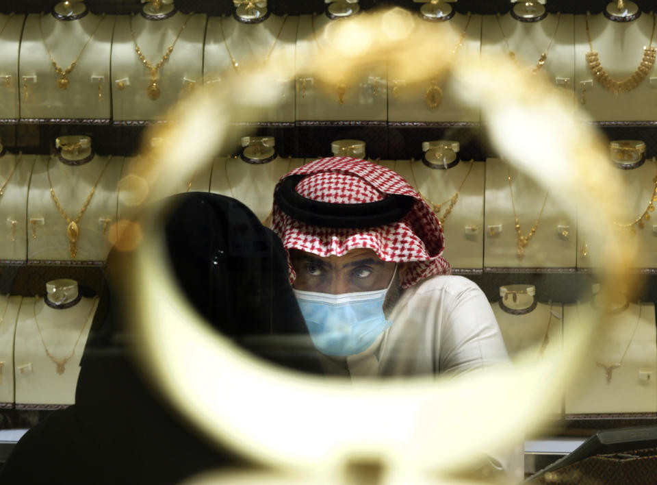 A Saudi vendor is seen through a bracelet as a woman buys jewels at the gold market a day before the expected increase of VAT from 5% to 15%, in Jiddah, Saudi Arabia, Tuesday, June 30, 2020. (AP Photo/Amr Nabil)