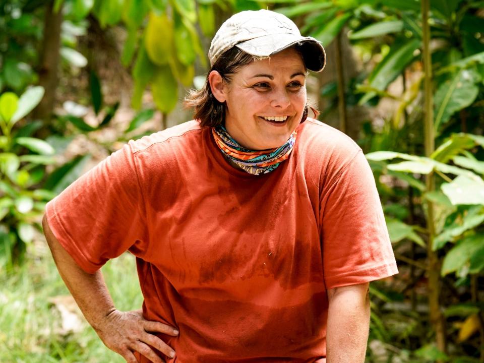 Elaine Stott on Survivor wearing a red shirt and hat in front of a forest