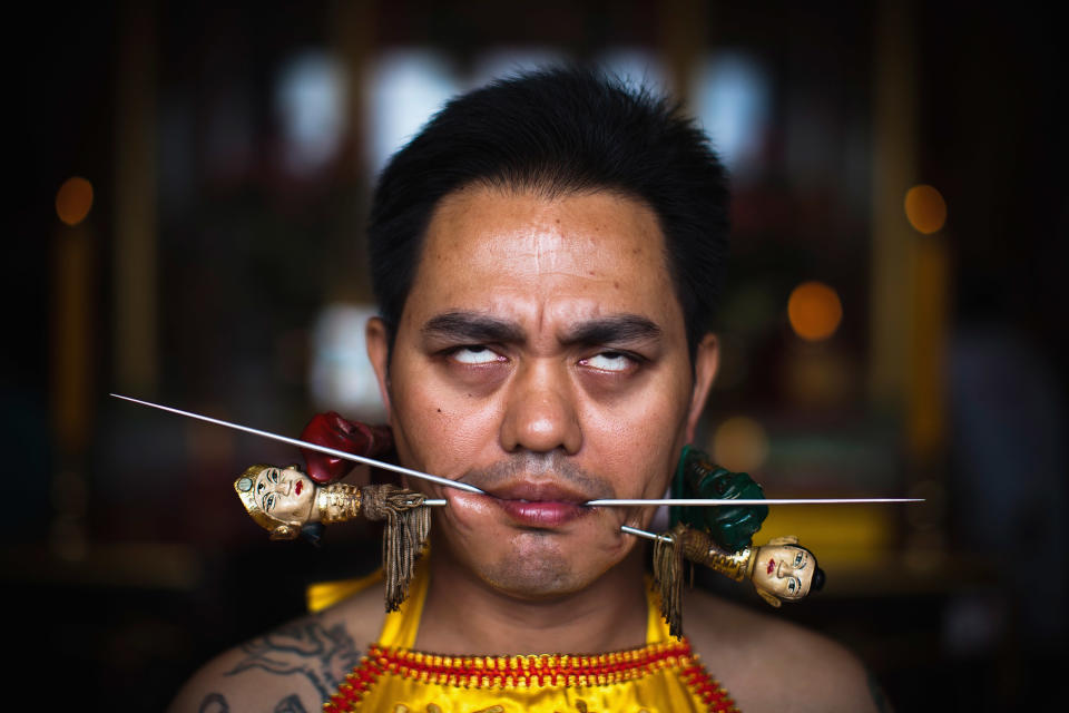 PHUKET, THAILAND - OCTOBER 05: A devotee of the Chinese shrine of Sui Boon Tong Shrine, pierces his cheeks with skewers during a procession of Vegetarian Festival on October 5, 2011 in Phuket, Thailand. Ritual Vegetarianism in Phuket Island traces it roots back to the early 1800's. The festival begins on the first evening of the ninth lunar month and lasts for nine days. Participants in the festival perform acts of body piercing as a means of shifting evil spirits from individuals onto themselves and bring the community good luck. (Photo by Athit Perawongmetha/Getty Images)