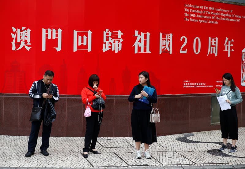 People stand in front of a poster celebrating the 20th anniversary of the former Portuguese colony's return to China in Macau